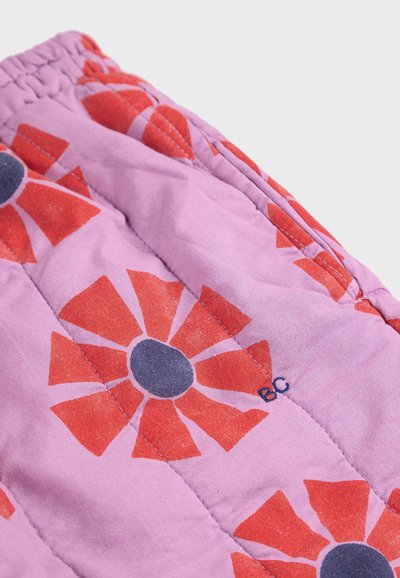 Tissu matelassé rose avec de grands motifs de fleurs rouges et des centres bleu foncé ; présente des coutures visibles et un petit détail brodé "BC".