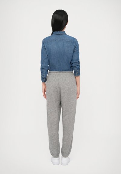 Džínová košeľa s dlhými rukávmi a gombíkovými manžetami, skombinovaná so sivými zúženými teplákmi a bielymi topánkami, zobrazená zozadu na jednofarebnom pozadí.