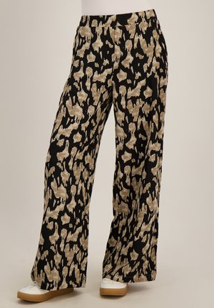Loszittende broek met zwart en beige abstract patroon, elastische tailleband, gedragen met witte sneakers met rubberen zolen.