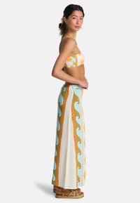 Σετ δύο τεμαχίων με τοπ μπαντό με ηλιακά μοτίβα σε πορτοκαλί και κρεμ, συνδυασμένο με φούστα ψηλόμεση, ροή με κύματα.