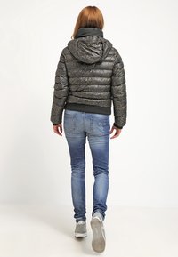 Kurtka puchowa w ciemnoszarym kolorze z teksturowanym wykończeniem, wyposażona w kaptur i elastyczne mankiety. Połączona z jasnoniebieskimi dżinsami i szarymi tenisówkami.