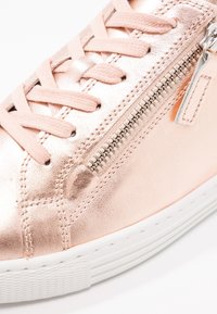 Baskets métalliques or rose avec lacets roses et fermeture éclair argentée sur le côté, dotées d'une semelle en caoutchouc blanche avec une adhérence texturée.