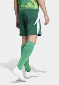 Green athletic shorts with white side stripes, matching green socks, and white football cleats. The jersey features a textured green design.