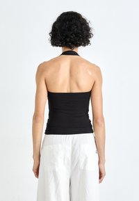 Black halter top with a fitted design, smooth fabric, and a straight hem, paired with white wide-leg pants featuring two large back pockets.