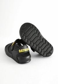 Mustad mustad, millel on tekstureeritud tallad, ning rihmal kollane "BATMAN" logo. Reguleeritav Velcro sulgur. Kerge disain.