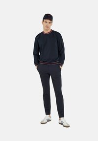 Granatowy sweter z dekoltem i mankietami w paski, zestawiony z dopasowanymi granatowymi spodniami. Białe sneakersy z szarymi i niebieskimi akcentami uzupełniają całość.