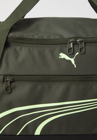 Olijfgroen stoffen sporttas met twee ritscompartimenten, voorzien van een zwarte bodem en een lichtgroen streepjespatroon met een Puma-logo.