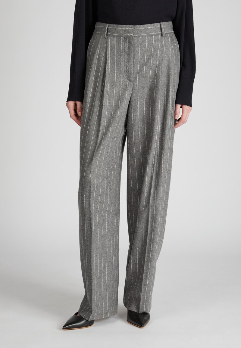 Pantalon à rayures grises en tissu texturé, avec taille haute, jambes larges et plis, associé à des chaussures noires à bout pointu.