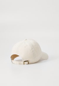 Fehér pamut baseball sapka ívelt viselési széllel, hátul állítható pánttal és diszkrét varrási részletekkel.