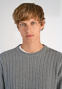 Szary, dzianinowy sweter o prążkowanej fakturze, okrągłym dekolcie, prezentujący casualowy styl. Modelka ma jasne włosy i niebieskie oczy.