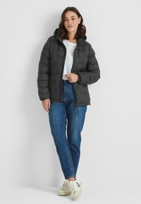 Black puffer jacket with a hood, featuring a quilted design and front zipper. Paired with blue jeans and cream sneakers.
