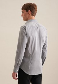 Camicia grigia con colletto, maniche lunghe e orlo curvo. Realizzata in tessuto morbido, presenta bottoni frontali e sui polsini.