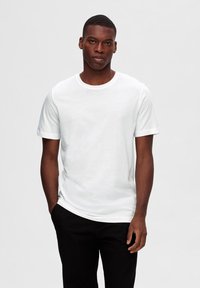 Camiseta blanca de manga corta en algodón con cuello redondo y corte relajado, combinada con pantalones negros. Textura suave, diseño liso, sin patrones.