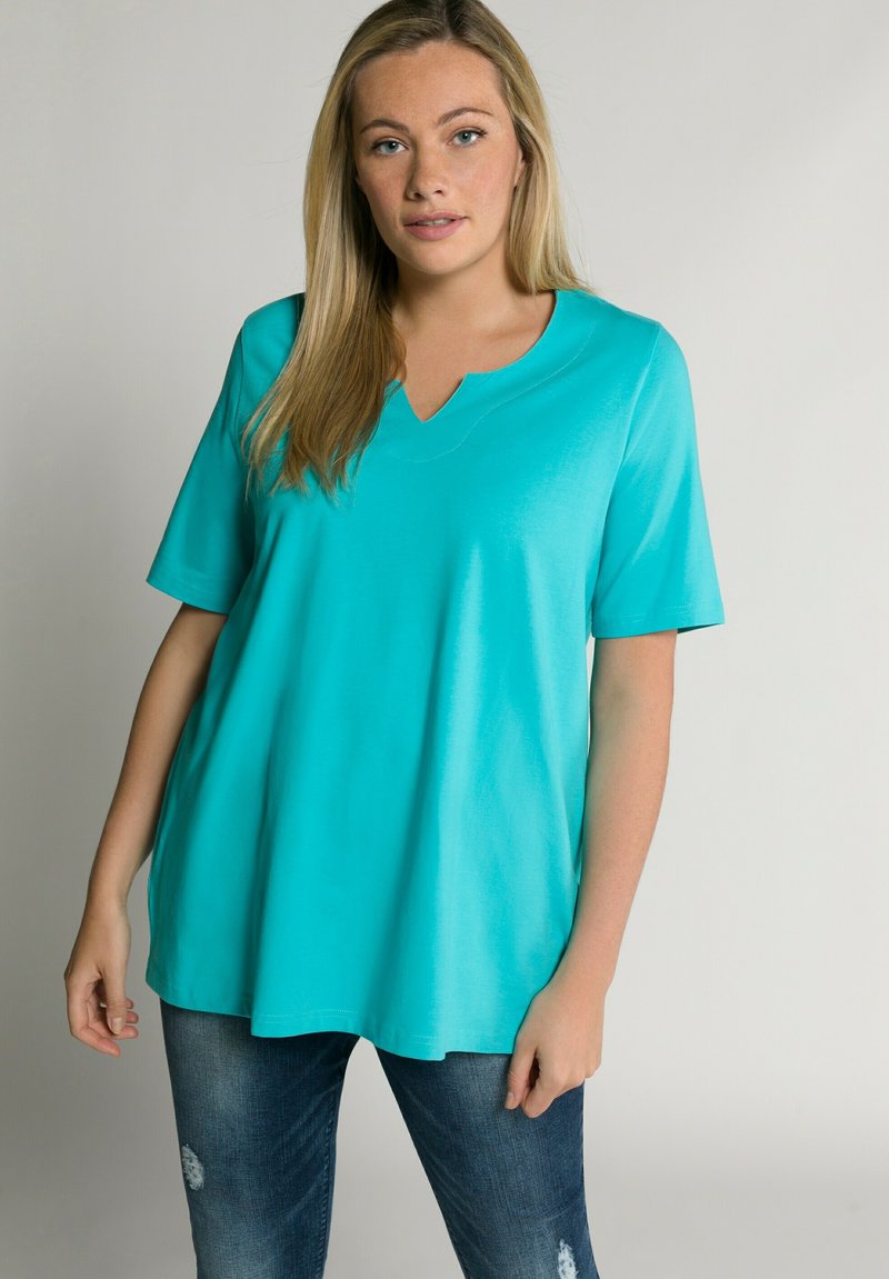 T-shirt turchese a maniche corte con scollatura a V in morbido tessuto, caratterizzato da una vestibilità comoda e una consistenza liscia, abbinato a jeans in denim strappati.