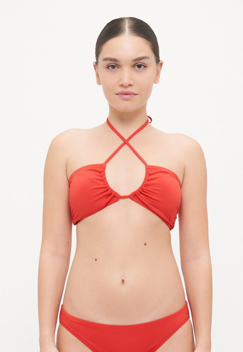Piros bikini szett sima anyagból. A top hátul ráncolt elülső résszel és keresztbe fonott pántokkal rendelkezik. Az alsó rész egyszerű, klasszikus szabású.