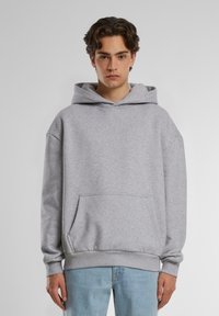 Grå hettegenser med kengurulomme, løs passform, ribbestrikkede ermer og nederkant. Laget av myk, teksturert stoff, som komplimenterer lyseblå jeans.