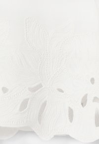 Tissu blanc avec broderie florale en relief et détails découpés formant des motifs complexes de pétales et de feuilles.