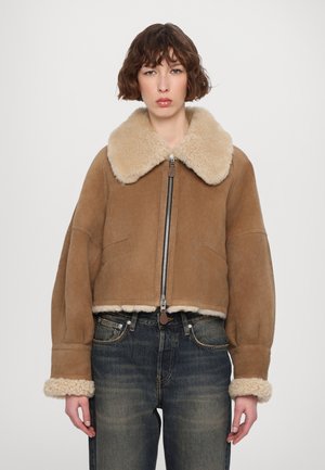 Bruine schapenvachtjas met een grote, fluffy beige kraag en manchetten. Voorzien van een ritssluiting aan de voorkant en zijzakken. Getextureerd, warm materiaal.