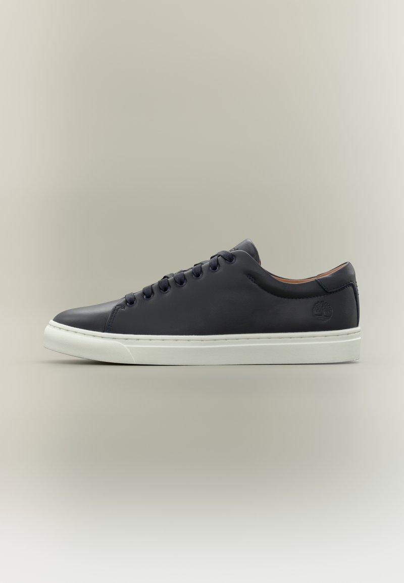 Μαύρο δερμάτινο παπούτσι τύπου sneaker χαμηλού προφίλ με μαύρα κορδόνια, λευκή σόλα και ανάγλυφο λογότυπο δέντρου στη φτέρνα, φωτογραφημένο σε ουδέτερο φόντο.