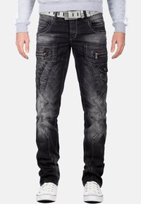 Verbleekte zwarte denim jeans met een slim fit, ritssluitingen aan de zijkant, contrasterende stiksels en een "Popular" logo op de dij. Gecombineerd met witte sneakers.