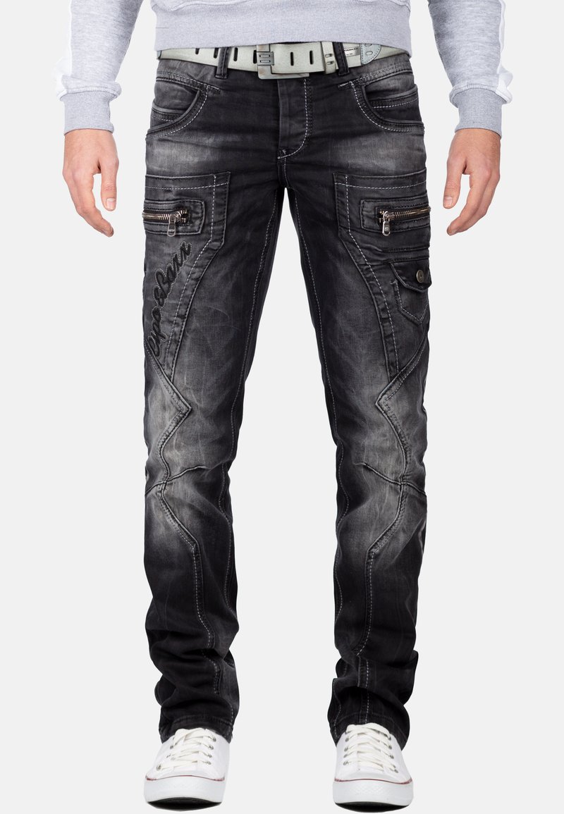 Verbleekte zwarte denim jeans met een slim fit, ritssluitingen aan de zijkant, contrasterende stiksels en een "Popular" logo op de dij. Gecombineerd met witte sneakers.