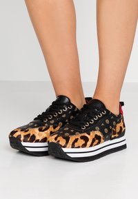 Baskets noires et imprimé léopard avec un dessus texturé, des accents de logo dorés et une semelle épaisse à rayures blanches et noires.
