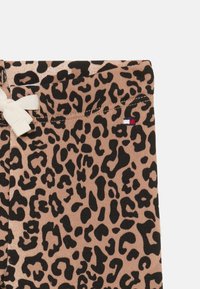 Leopardskinnöbel med sydd midjeband och liten vit rosett på vänster sida, med en liten röd, vit och blå logotyp.