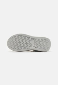 Sneakersåle laget av gummimateriale, grå farge, teksturert for grep, med en sikksakkmønster og preget merking.