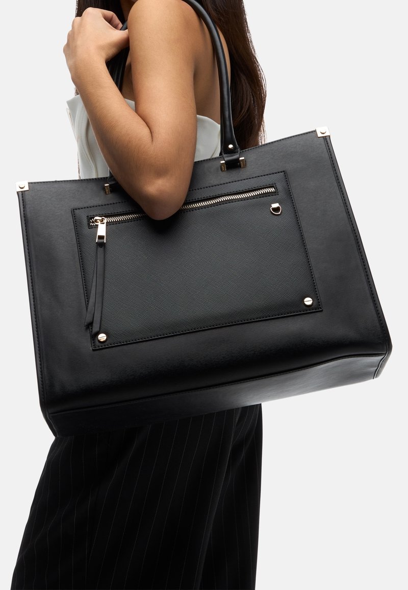 Borsa a tracolla nera in pelle testurizzata, con una tasca frontale con zip e hardware dorato. Forma rettangolare con manici lunghi.