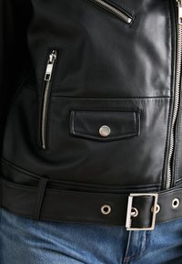 Must must have nahkjakke, millel on hõbedased tõmblukud, nööpkott ja vöö, millel on klamber, ning sellele on lisatud õmblusi ja auke.