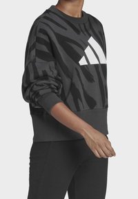 Felpa nera con stampa animale testurizzata, grande logo Adidas bianco, polsini a coste e orlo cropped. Tessuto morbido e spesso.