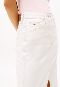 Jupe crayon en denim blanc avec fente latérale, comprenant des coutures légères, des poches standard et une étiquette en cuir de marque à l'arrière.
