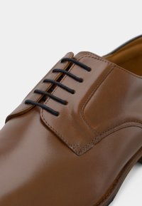 Braune Leder Schuhe mit glänzender Oberfläche, ausgestattet mit schwarzen Schnürsenkeln, einer glatten Textur und einem strukturierten Zehendesign. Klassischer formeller Stil.