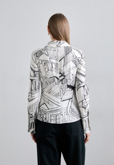Blazer blanco con patrones arquitectónicos negros, con un corte entallado y mangas largas, combinado con pantalones oscuros, visto desde la parte posterior.