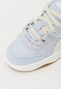Baskets de sport bleu clair avec des matériaux en maille et en cuir, dotées de lacets beiges, d'un motif texturé et d'une semelle intermédiaire blanche.