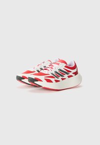 Scarpe da ginnastica rosse con tomaia in rete, dettagli in bianco e nero, suola arrotondata e una presa testurizzata sulla suola esterna.