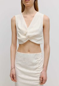 Weißes, ärmelloses Crop-Top mit einem gedrehten Vorderdesign, kombiniert mit einem engen Bleistiftrock mit Raffung und strukturiertem Blumendesign.