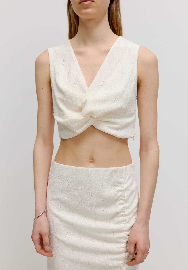 Weißes, ärmelloses Crop-Top mit einem gedrehten Vorderdesign, kombiniert mit einem engen Bleistiftrock mit Raffung und strukturiertem Blumendesign.