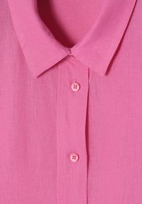 Chemise en lin rose avec un col classique, deux boutons roses et un tissu léger et texturé. Design simple et épuré.