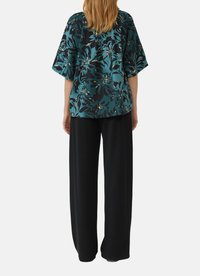 Haut à imprimé floral en teal et noir avec une coupe décontractée et de larges manches, associé à un pantalon noir ample.