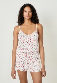 Ensemble de pyjama blanc avec un imprimé floral de roses rouges. Le haut a une finition en dentelle et des bretelles spaghetti ajustables ; le short a une taille élastique.