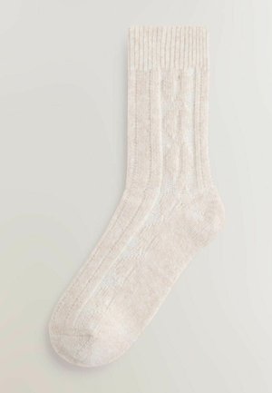 Gestrickte Knöchelsocke in hellbeige mit geripptem Bündchen. Verfügt über ein dezentes Kabelmuster und eine weiche, strukturierte Oberfläche.