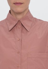 Hemd mit Knöpfen in einem sanften Mauve-Ton, ausgestattet mit einem klassischen Kragen, einer Brusttasche und einem glatten, leichten Stoff mit einem leichten Glanz.