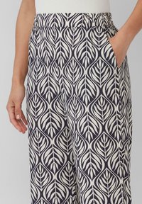 Spodnie w kolorze granatowym i kremowym z wzorem liściowym, z elastycznym pasem i kieszeniami bocznymi. Materiał wydaje się lekki i gładki.