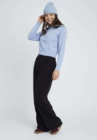 Pull bleu clair en tricot avec un col zippé, associé à un pantalon large noir et des chaussures bordeaux. Bonnet de couleur bleue assortie.