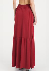 Gonna maxi rossa con vita arricciata, design a strati e tessuto morbido. La gonna arriva fino alle caviglie, con una silhouette fluida e dettaglio spaccato.