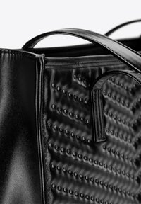 Czarna torba ze skóry z teksturowaną powierzchnią z wypukłymi kropkami, dwoma solidnymi uchwytami i eleganckim designem. Materiał ma błyszczące wykończenie.