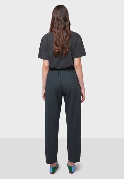 Pantaloni neri a vestibilità ampia con vita elastica, abbinati a una t-shirt grigio scuro con maniche corte e scarpe multicolori, visti da dietro.
