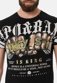 Schwarzes Baumwoll-T-Shirt mit auffälligem grafischen Design, erhobenen Buchstaben und illustrierten Fäusten, die Geldscheine, Ringe und das Dollarzeichen halten.