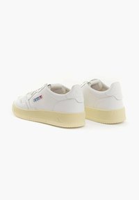 Scarpe da ginnastica in pelle bianca con suole in gomma beige. Presentano cuciture dettagliate e un logo sul lato. Punta tonda e design con lacci.